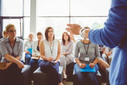 Hand of a trainer addressing group of females sitting in a conference hall. Female hand against defocused group of women attending seminar.