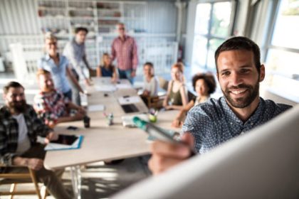 Happy businessman writing a business plan on whiteboard to his team on a meeting in board room.