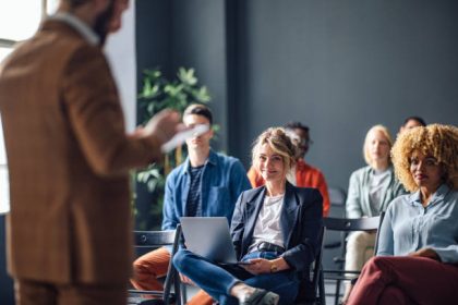 Group of men and women sitting and listening to a seminar. They are smiling.